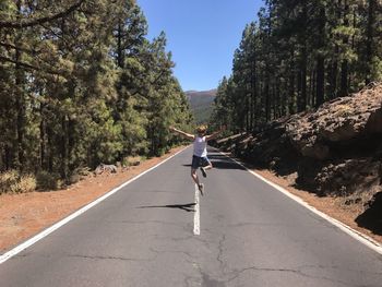 Rear view of excited woman jumping on road during sunny day