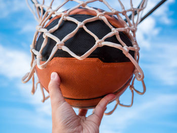 Cropped hand playing basketball against sky