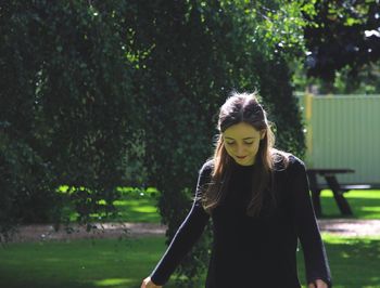 Young woman standing on grass against trees