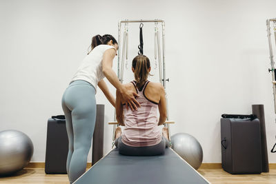 Fitness instructor assisting woman in practicing exercise on reformer