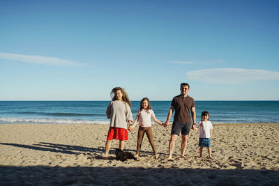 Rear view of big family with two girl and a dog walking at beach against sky