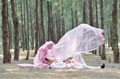 Rear view of woman sitting on tree trunk in forest