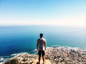 Rear view of man standing at lion head over city while looking at horizon