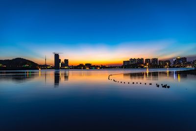 Reflection of silhouette buildings in blue river against clear sky at dusk