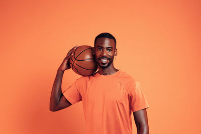 Portrait of young man standing against orange background