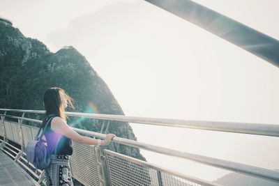 Rear view of woman standing by railing against clear sky