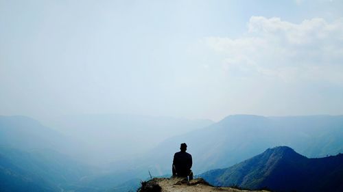 Rear view of man sitting against mountains