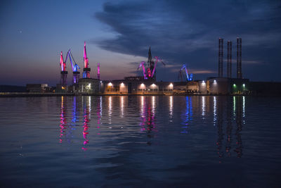 Illuminated city by river against sky at night