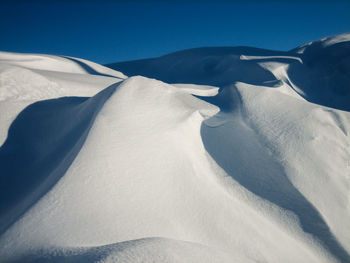 Snow dunes on a desolate glacier with no people, strong shadows and blue sky