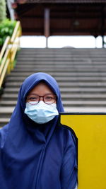 Portrait of a girl wearing blue hijab, sunglasses and disposable mask standing outdoors