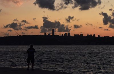Rear view of man standing by sea against sky during sunset