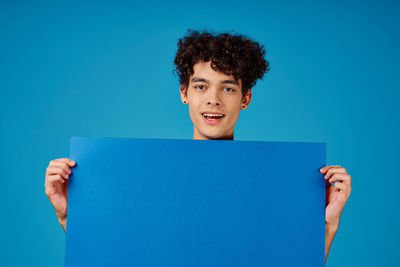 Portrait of teenage boy holding paper against blue background