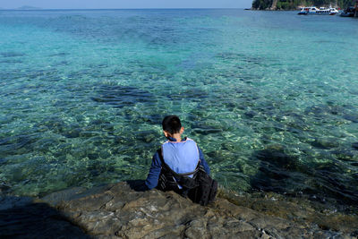 Rear view of man sitting on rock by sea