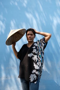 Mature woman holding asian style conical hat against wall