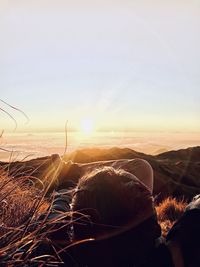 Rear view of man relaxing against sky during sunset