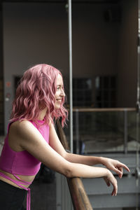 Smiling woman with pink hair standing by railing