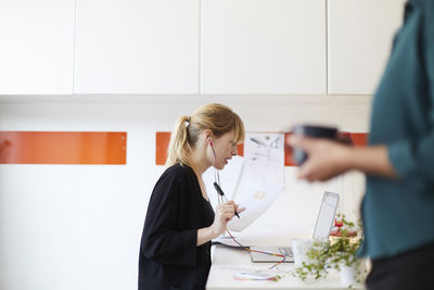 Side view of mid adult businesswoman working at table with colleague in foreground at office