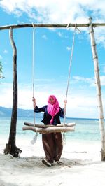 Rear view of woman sitting on swing at beach against sky