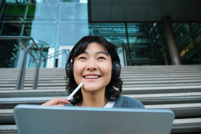 Portrait of young woman using mobile phone while standing in office