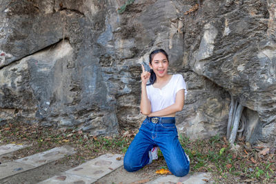 Portrait of smiling young woman kneeling against rock formation