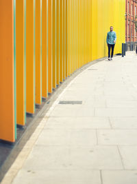 Man walking on footpath by modern yellow building in city