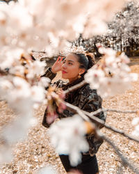 Smiling young woman looking away while standing by cherry blossom tree during winter