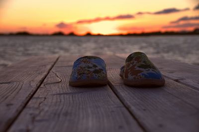 Close-up of shoes on wood against sky during sunset