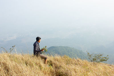 Young man using mobile phone while standing on mountain against sky