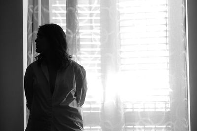 Woman looking through window at home