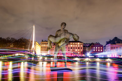Illuminated statue by city against sky at night