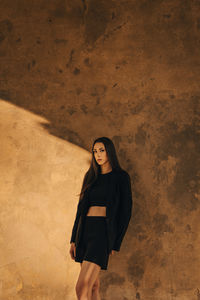 Portrait of young woman standing against wall