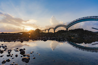 Bridge over water against sky during sunset