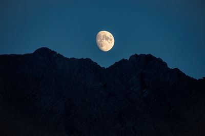 Low angle view of moon behind mountainrange against sky at night