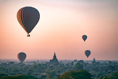 Hot air balloons flying over landscape against sky during sunset