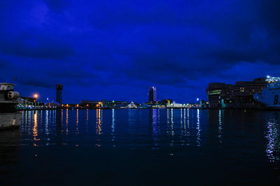 Illuminated cityscape by sea against sky at night