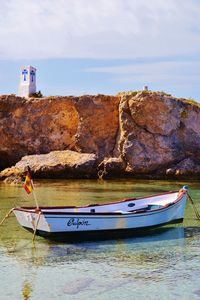 Boat moored at sea by rock formation against sky