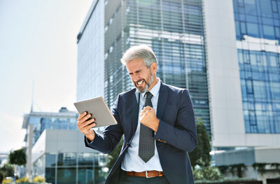 Businessman using digital tablet while standing outside office building