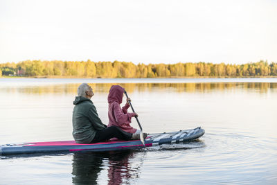 Senior man with granddaughter paddleboarding in lake