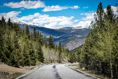 Road amidst trees and snowcapped mountains against sky