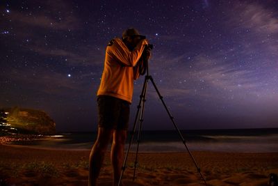 Rear view of person photographing sea against sky at night