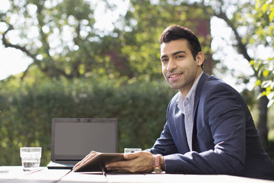 Portrait of smiling businessman with laptop at outdoor cafe