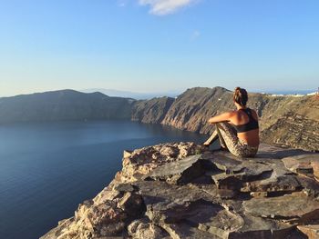 Rear view of woman sitting on rock by sea against clear sky