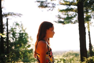 Side view of young woman standing against trees in forest