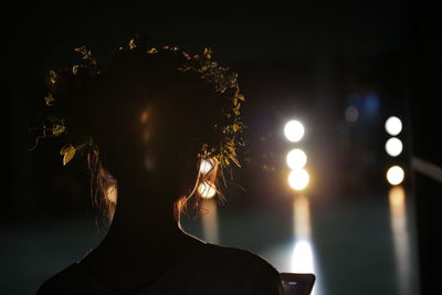 Close-up of silhouette woman against sky and illuminated lights at night