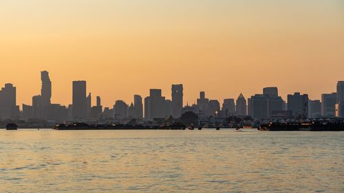 Sea by buildings against sky during sunset