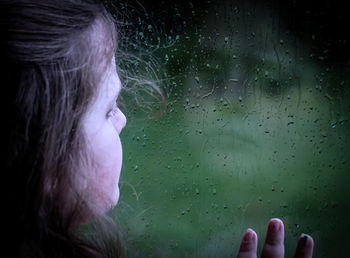 Close-up of girl looking through wet window during rainy season