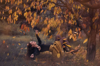 Young woman flying under autumn tree on field