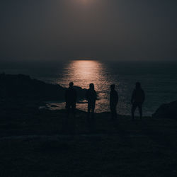 Silhouette people on beach against sky during sunset