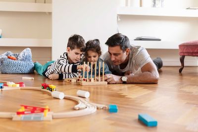 Children playing with toy block while lying down with father on hardwood floor