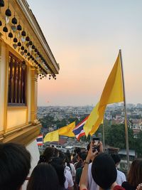 People with flags in city against sky during sunset